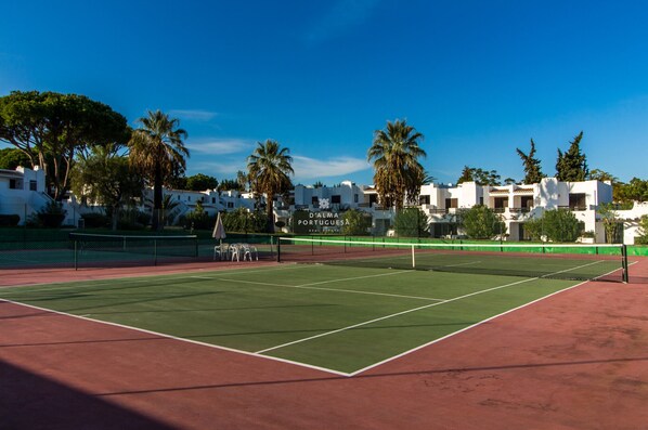 Un court de tennis avec un filet, entouré de bâtiments et de palmiers.