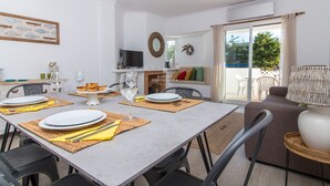 Comedor con mesa dispuesta para cuatro, un televisor y un sofá al fondo.