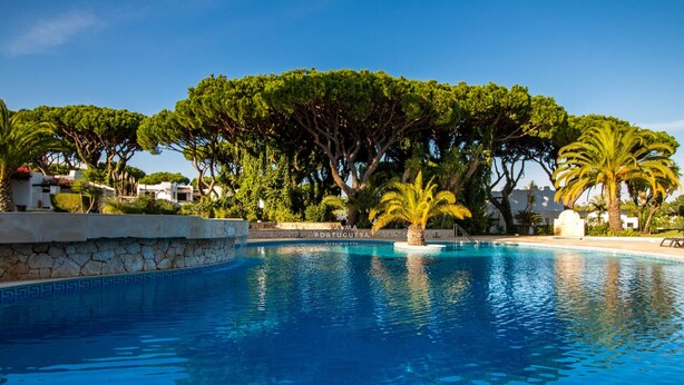 Una piscina con borde de piedra, rodeada de árboles y un cartel que dice 'PORTUGUESA'.