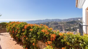 A terrace with a view of a mountainous landscape, a stone wall with flowering plants, and a building with a tiled roof. - Holiday Home "Casa Rural Villena" with Sea View, Wi-Fi, Pool & Terrace (Frigiliana)