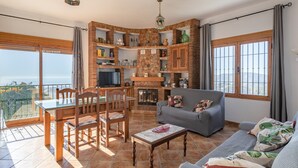 A living room with a fireplace, a dining area, and a balcony with a view. - Holiday Home "Casa Rural Villena" with Sea View, Wi-Fi, Pool & Terrace (Frigiliana)