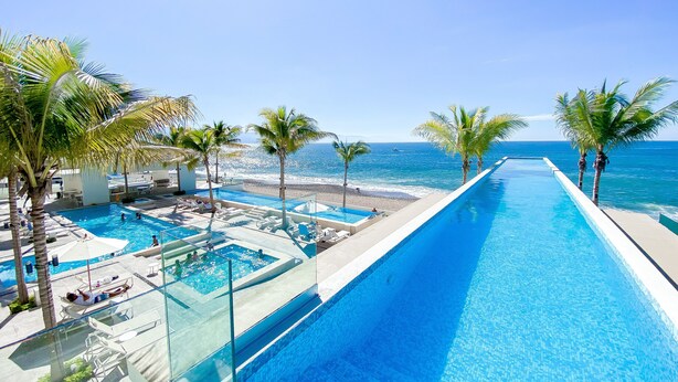 A pool area with clear blue water, palm trees, and a view of the ocean. - L'Armatore LOFT"- Italian Style (Puerto Vallarta)