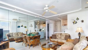 A spacious living area with wicker furniture, a glass coffee table, and a view of the ocean.