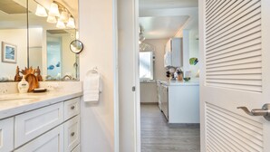 A modern bathroom with a large mirror, white cabinetry, and a wooden decorative piece.