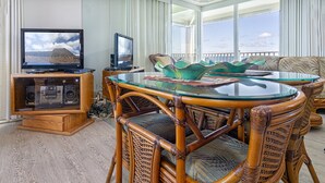 A room with a glass-top table surrounded by wicker chairs, a television, and a speaker system.