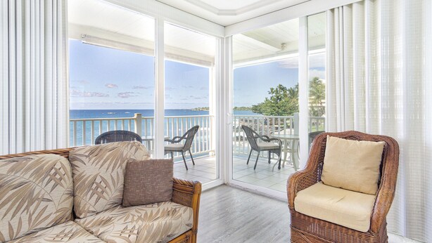 A balcony with a view of the ocean, wicker furniture, and a glass door leading to the outdoor area.