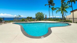 Ein Pool mit geschwungener Kante, umgeben von Liegestühlen und Palmen, mit Blick auf das Meer.