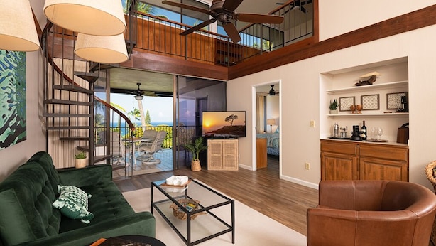 A spacious living area with a green sofa, a leather armchair, and a coffee table. A staircase leads to an upper level with a balcony.