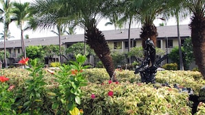 A landscaped garden with various plants and a statue, surrounded by a building with multiple balconies and a staircase.