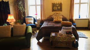Ein gemütliches Schlafzimmer mit einem großen Bett, einer Sitzecke mit Sessel und Tisch, einer Chandelieber und einem Fenster mit Vorhängen.