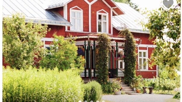 Ein rotes Holzhaus mit Veranda, umgeben von üppiger Vegetation.