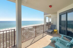 Varanda com vista para a praia, uma cadeira, uma mesa pequena e uma porta de vidro.