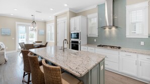 A spacious kitchen with a large island, white cabinetry, and a stainless steel range hood.