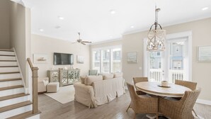 A spacious living room with a large sofa, a dining table with wicker chairs, a ceiling fan, and a chandelier.