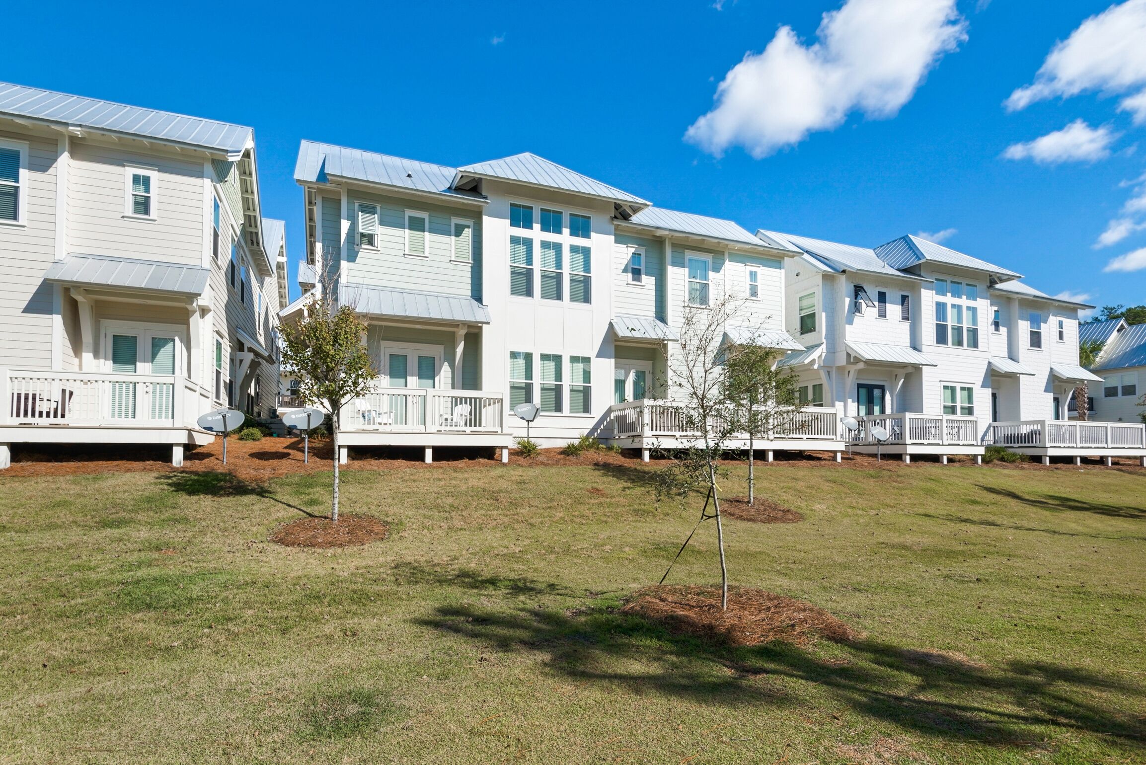 A row of white townhouses with balconies, satellite dishes, and small trees in the yard.