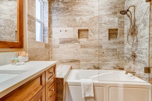 A bathroom with a marble wall, a bathtub, a shower, and wooden cabinetry.
