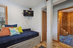 A room with a sofa, a television mounted on the wall, a wooden door, and a patterned rug.