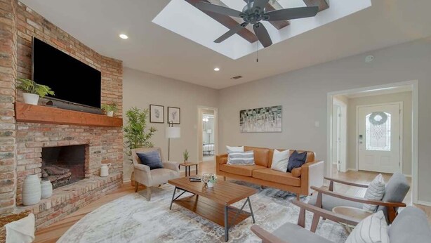 Un salon avec une cheminée en briques, un téléviseur à écran plat, un ventilateur de plafond et une grande fenêtre.