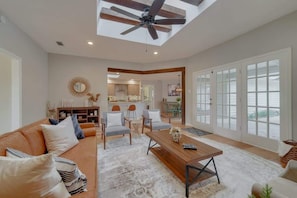 A spacious living room with a ceiling fan, a wooden coffee table, and a large window with a view. - Best of Richardson | 5BD/3BA with Pool, Patio, BBQ (Richardson)