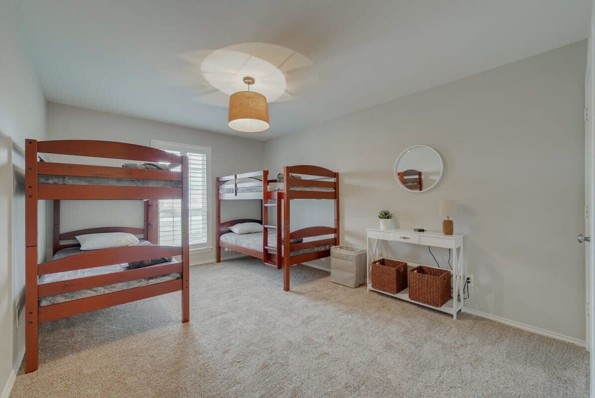 Een slaapkamer met stapelbedden, een klein wit bureau, een spiegel en een plafondventilator.