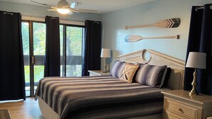 A bedroom with a large bed, two bedside tables, a ceiling fan, and a view of the outdoors.