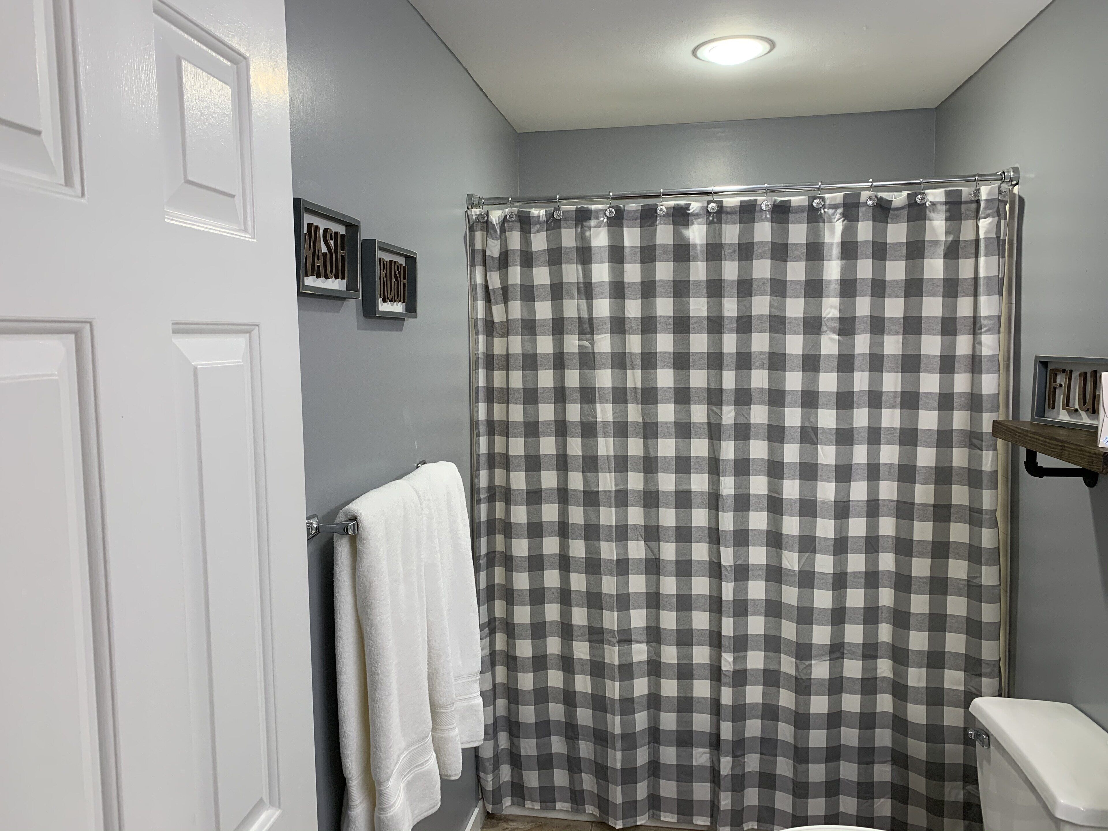 A bathroom with a checkered shower curtain, a white toilet, and a towel hanging on the wall.