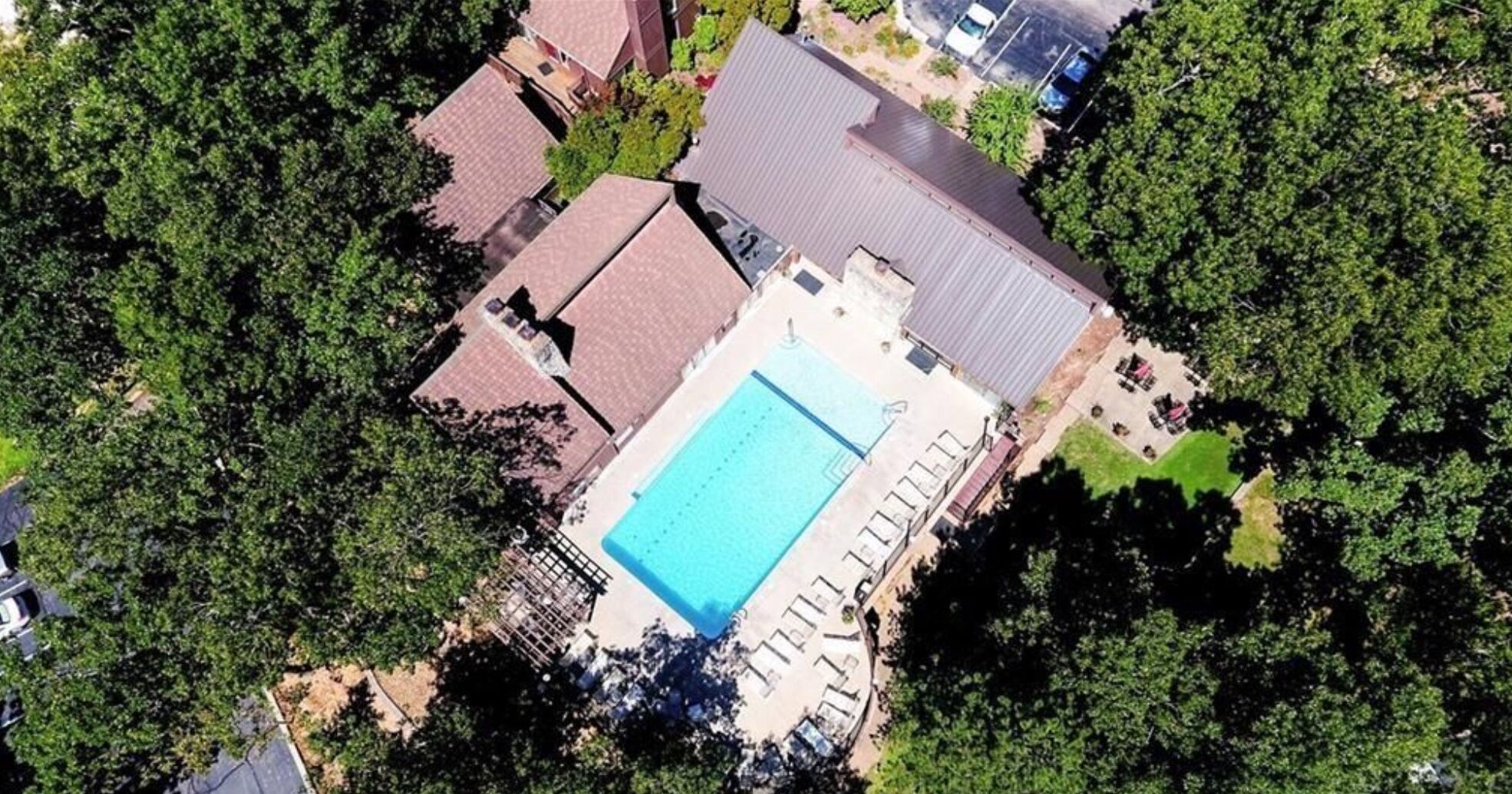 Vue aérienne d’un quartier résidentiel avec une piscine, plusieurs maisons et de nombreux espaces verts.