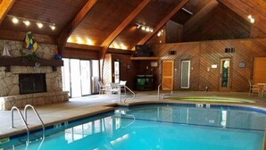 An indoor swimming pool with wooden beams, a stone fireplace, and a stone wall.