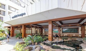 A hotel entrance with a covered outdoor area, a koi pond, and a large mural. - Waikiki condo - lanai, pool & beach access (Honolulu)