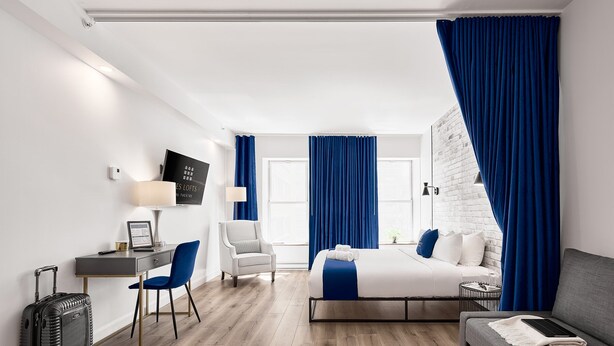 Een moderne hotelkamer met een bed, een bureau, een stoel, een bank en een koffer.