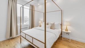 Un dormitorio moderno con cama con dosel, dos mesitas de noche con lámparas y un amplio ventanal con cortinas.
