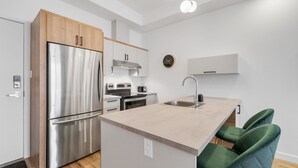 Una cocina moderna con un refrigerador de acero inoxidable, armarios de madera, un horno empotrado y un lavamanos. Hay dos sillas tapizadas en verde en la isla.