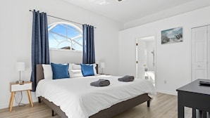 Ein Schlafzimmer mit einem großen Bett, einem Nachttisch, einem Schreibtisch und einem Fenster mit Vorhängen.