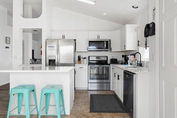 Une cuisine moderne avec des armoires blanches, des appareils en acier inoxydable et deux tabourets turquoise.