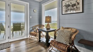 A room with a view of the ocean, wicker furniture, a table with a lamp, and a framed picture on the wall. - Experience island life with amazing views and easy beach access! 6BR, 5BA (Wrightsville Beach)