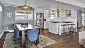 A modern kitchen with white cabinets, a central island with stools, and pendant lighting. - Experience island life with amazing views and easy beach access! 6BR, 5BA (Wrightsville Beach)