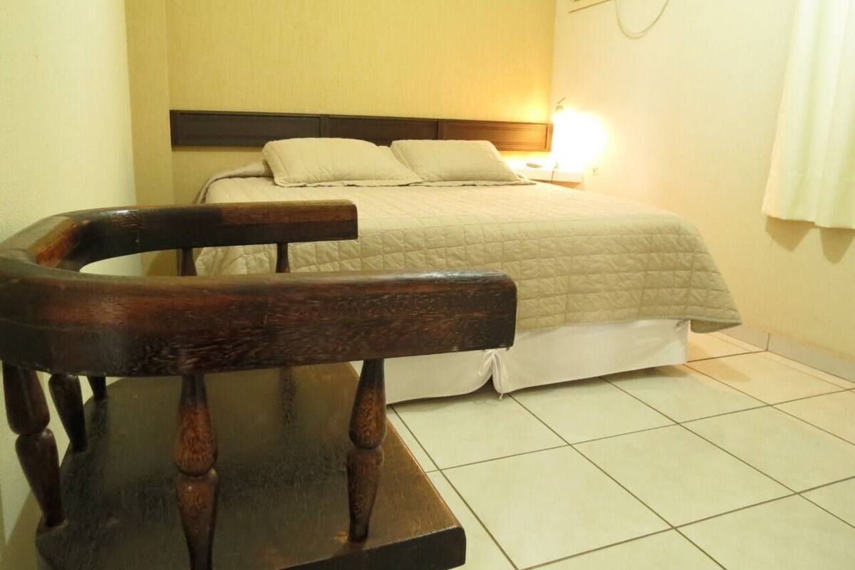 A bedroom with a bed, a wooden chair, and a bedside table.