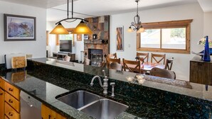 A kitchen with granite countertops, a dishwasher, and a dining area with wooden chairs and a table.