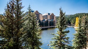 A lodge with multiple floors, a bridge over a lake, and dense forest surrounding it.