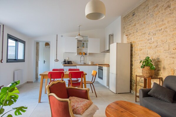 A modern kitchen with white cabinets, a wooden dining table with red chairs, and a stone wall. - Village house with terrace and small garden in the heart of Saint Pierre d'Oleron (Saint-Pierre-d'Oléron)