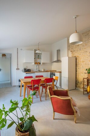 A modern kitchen with white cabinets, a dining area with red chairs, and a stone wall. - Village house with terrace and small garden in the heart of Saint Pierre d'Oleron (Saint-Pierre-d'Oléron)