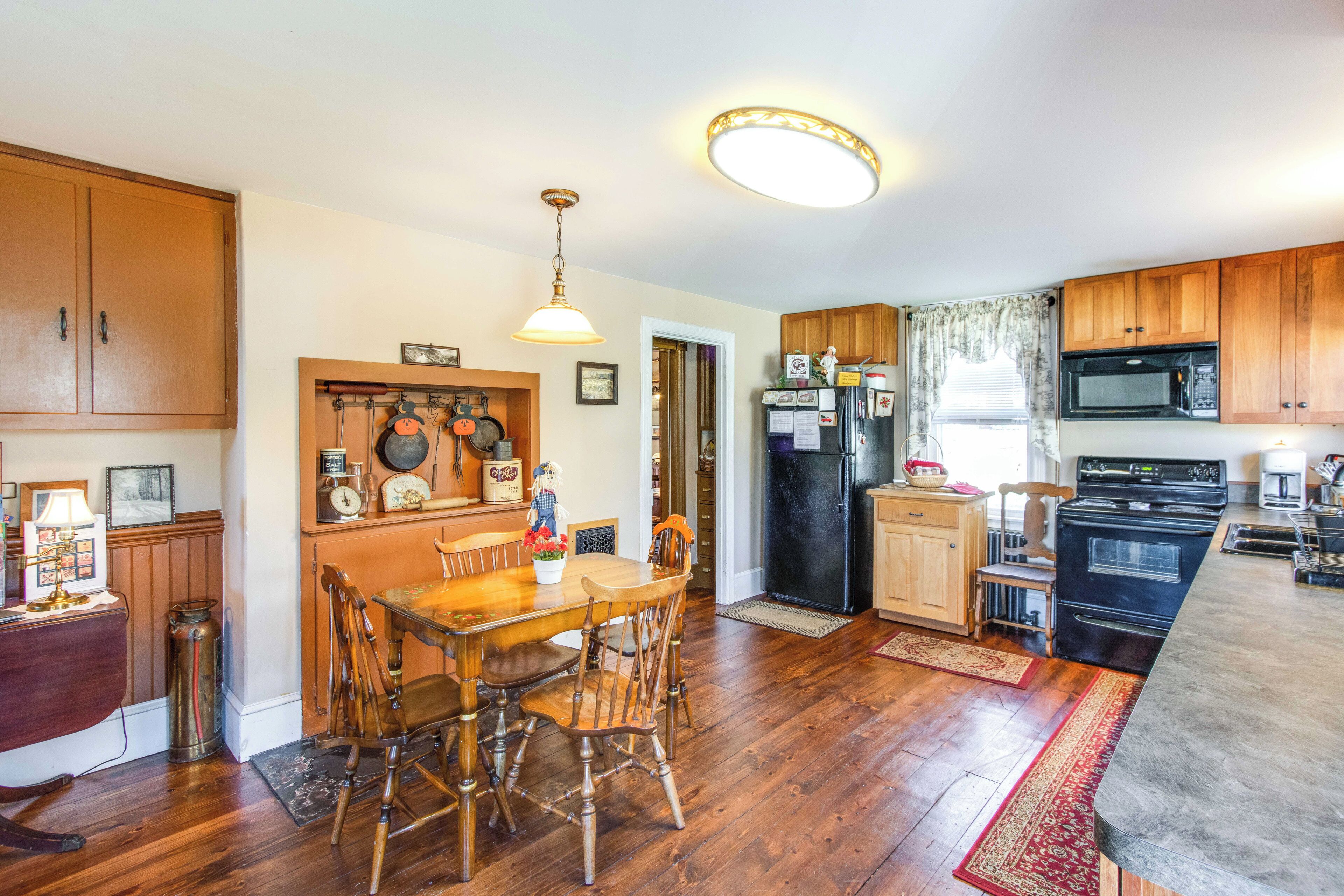 Una cocina con armarios de madera, una mesa de comedor con sillas, un refrigerador, un microondas y una estufa.