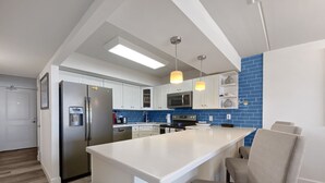 A modern kitchen with white cabinets, a stainless steel refrigerator, a microwave, and a large island with seating.
