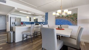 A modern kitchen with a central island, bar seating, and a dining area with a chandelier.