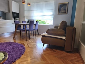 A modern kitchen with a dining area, a purple rug, and a brown chair.