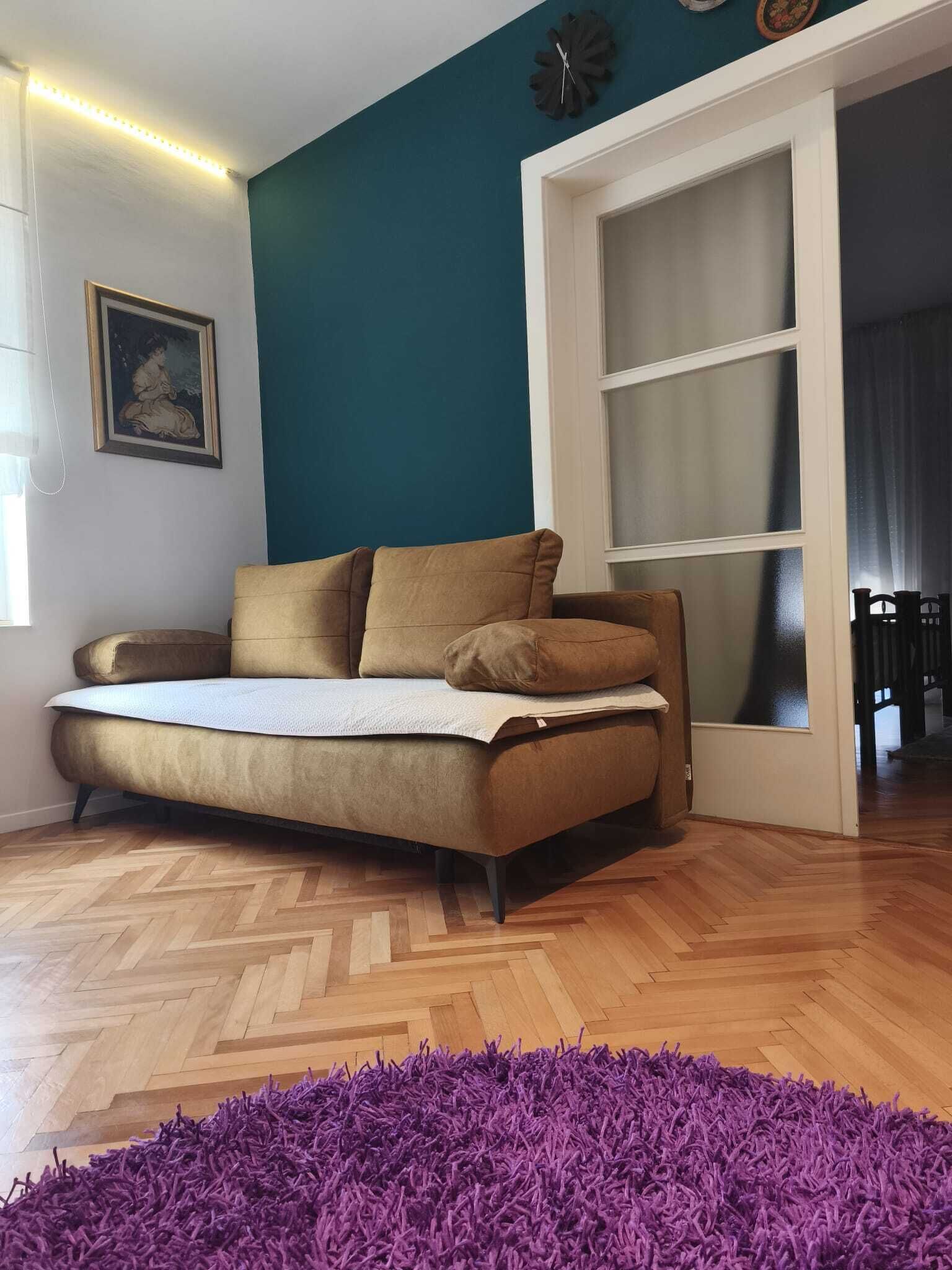 A room with a sofa, a purple rug, a clock, and a window.