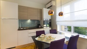 Una cocina moderna con comedor, que incluye una mesa negra, sillas moradas y vistas al exterior a través de grandes ventanales.