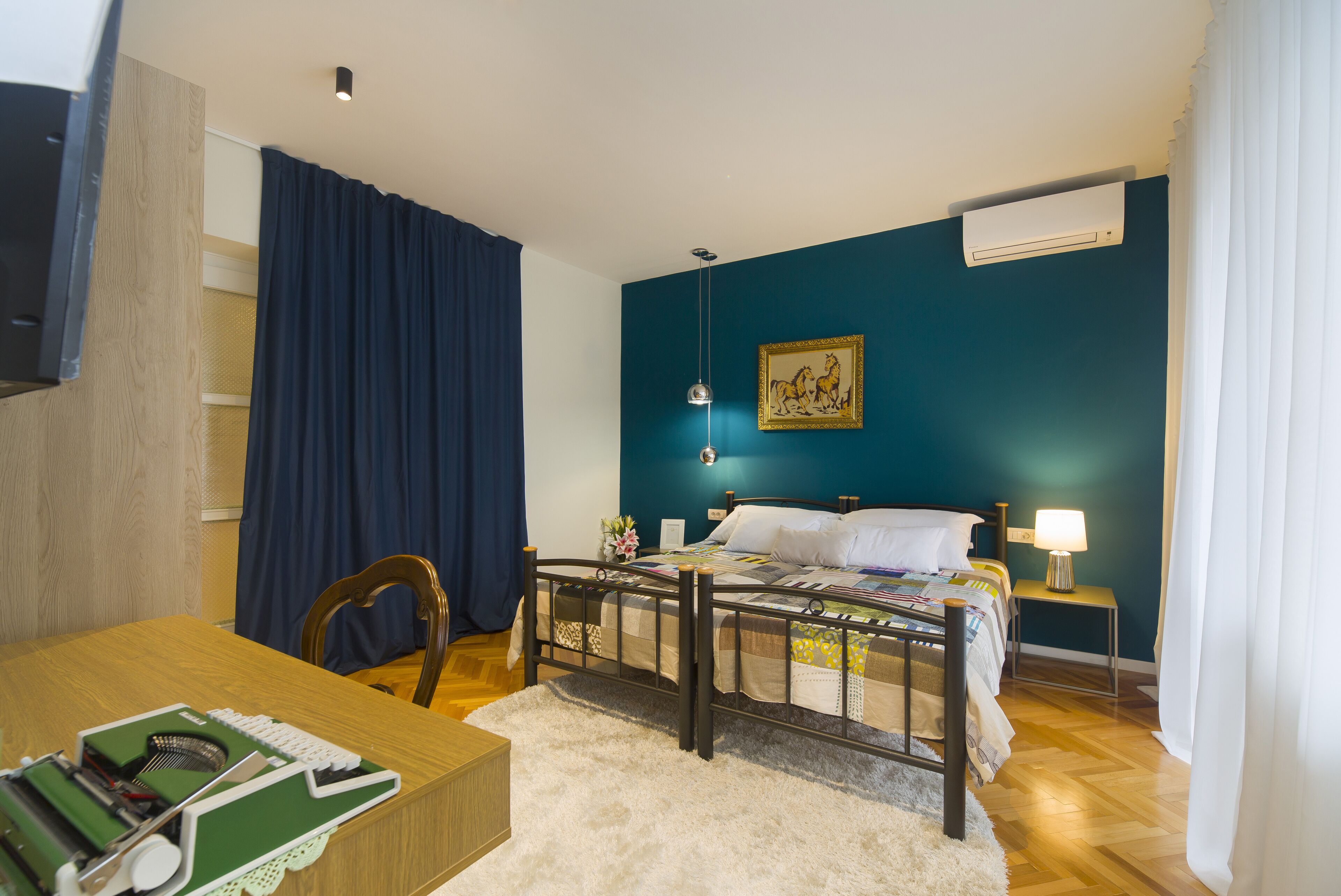 Une chambre à coucher comprenant un lit, un bureau, une chaise, une lampe et un appareil de climatisation.