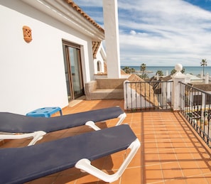 A balcony with two lounge chairs, a wicker sofa, and a view of the sea and buildings. - Marina Real apto 433 (Manilva)