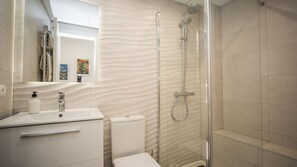 A modern bathroom with a glass-enclosed shower, a white sink with a soap dispenser, and a toilet.